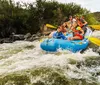 A group of excited people including children and adults wearing safety gear are white-water rafting in a turbulent river