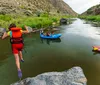 A group of excited people including children and adults wearing safety gear are white-water rafting in a turbulent river