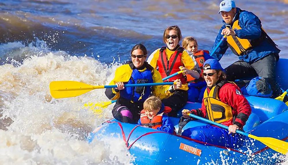 A group of excited people including children and adults wearing safety gear are white-water rafting in a turbulent river