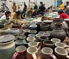 Two smiling people are seated at a pottery workshop surrounded by other participants engaged in ceramic making