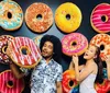 Three people are playfully interacting with large decorative doughnut designs on a wall