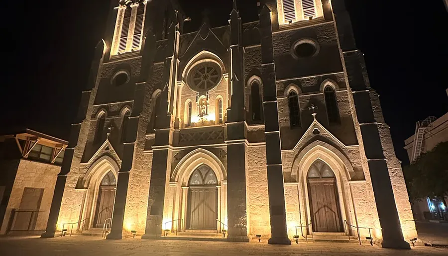 The image shows the illuminated facade of a Gothic-style church at night, creating a dramatic and historic architectural scene.