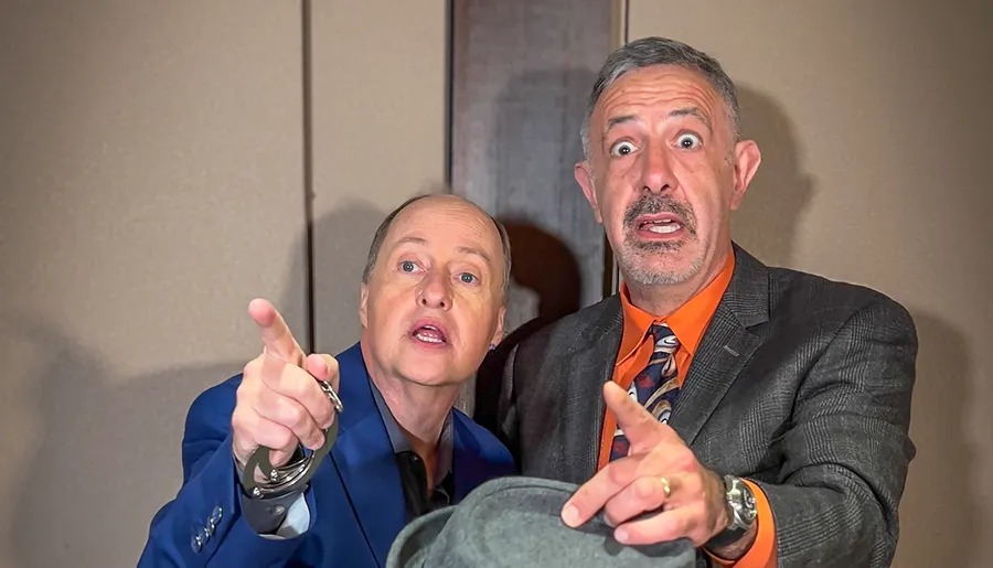 Two men are making surprised expressions and pointing towards something off-camera with one of them handcuffed, creating a humorous and intriguing scene.