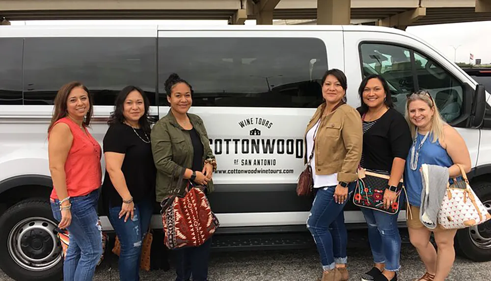 A group of six women pose smiling in front of a COTTONWOOD Wine Tours van