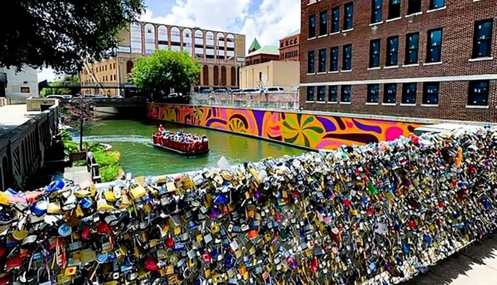 A colorful urban scene showing a river with a tour boat a vibrantly painted wall and a fence densely adorned with numerous love locks