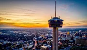 The image captures a breathtaking aerial view of a city at sunset with a prominent tower in the foreground, set against a vibrant sky.