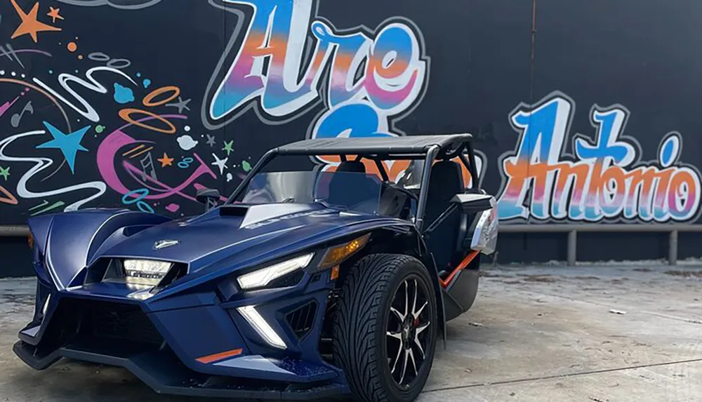 A blue three-wheeled vehicle is parked in front of a vibrant graffiti wall with the text Hire San Antonio