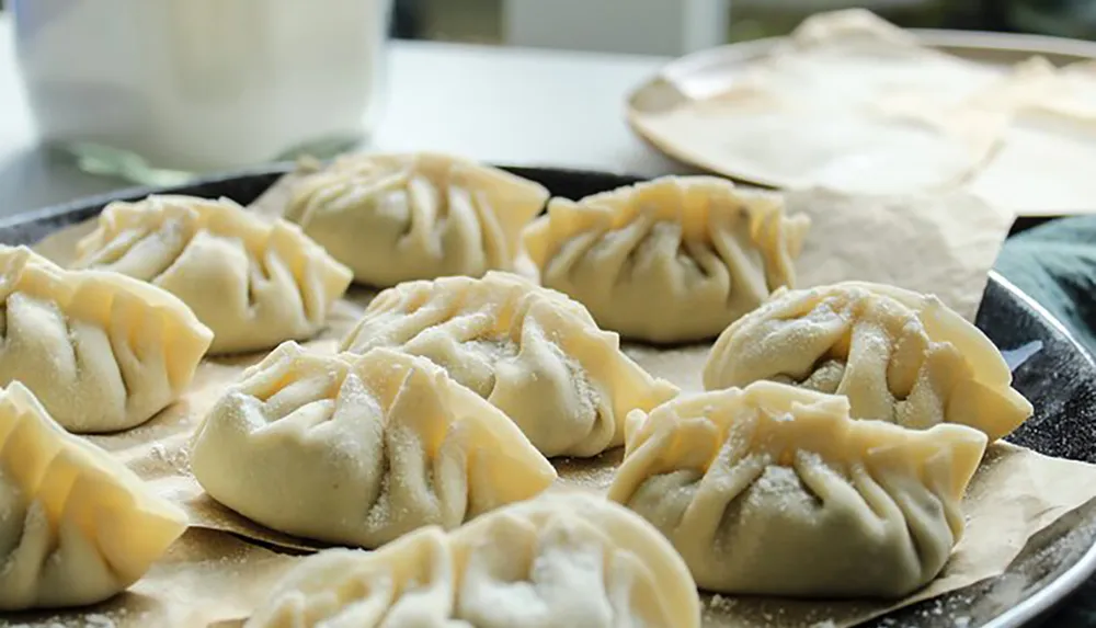 A tray of freshly made dumplings sits ready for cooking dusted with flour on parchment paper