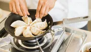 A person is pan-frying dumplings on a stovetop.