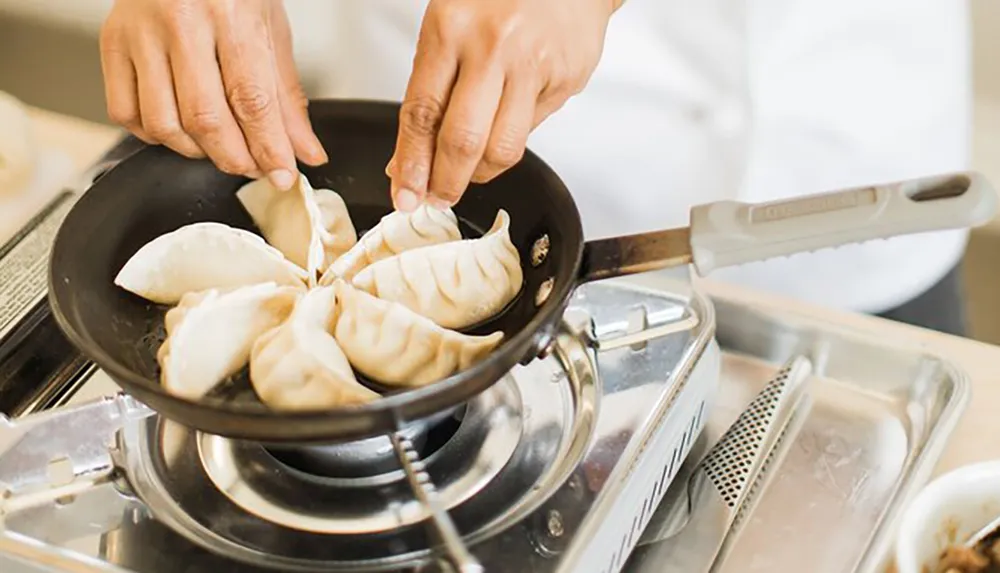 A person is pan-frying dumplings on a stovetop