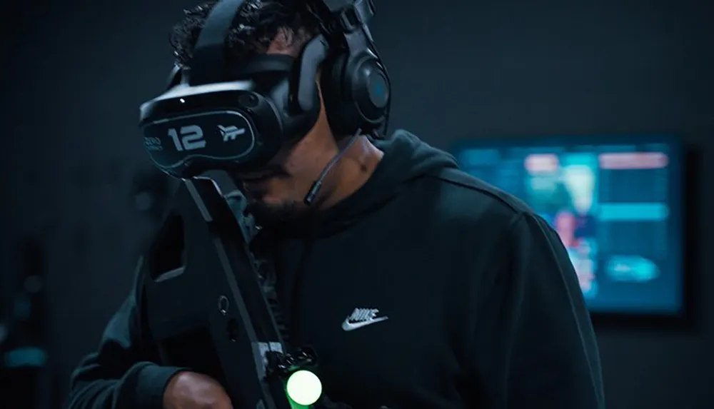 A person is engaged in a virtual reality experience wearing VR goggles and a headset while holding what appears to be a simulation gun with a blurred technology interface visible in the background