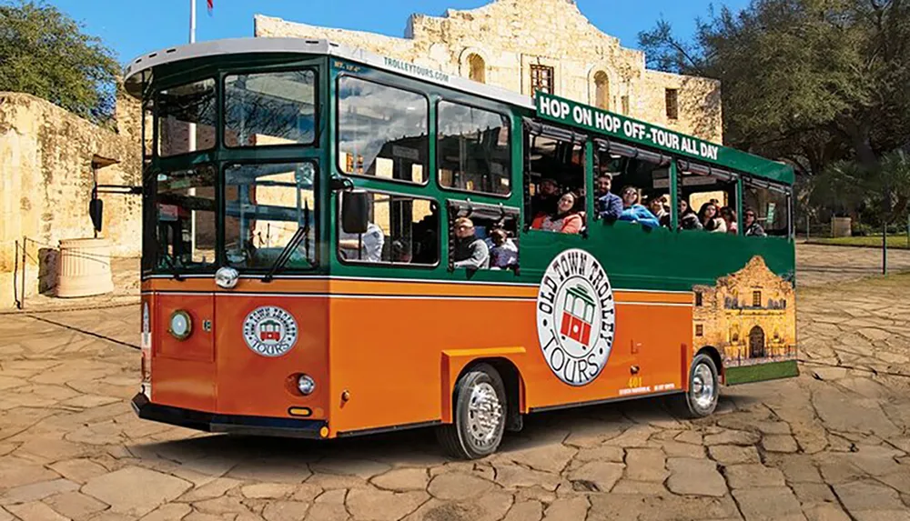 The image shows a colorful sightseeing trolley bus with passengers aboard indicating a hop-on-hop-off tour service under a clear sky with historical architecture in the background