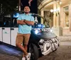 A person is standing confidently with arms crossed next to an electric shuttle vehicle on a city street at night