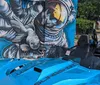 A blue and black three-wheeled vehicle is parked in front of a colorful mural that spells out SAN ANTONIO TEXAS