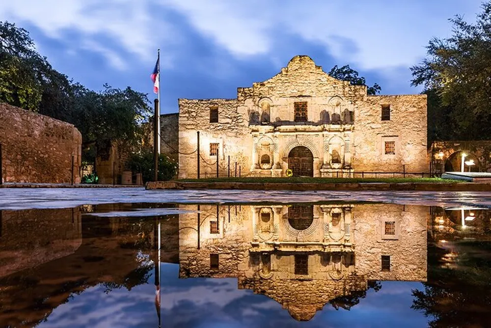 The Alamo Mission in San Antonio Texas is illuminated in the early evening and reflected in a smooth water surface in front of it