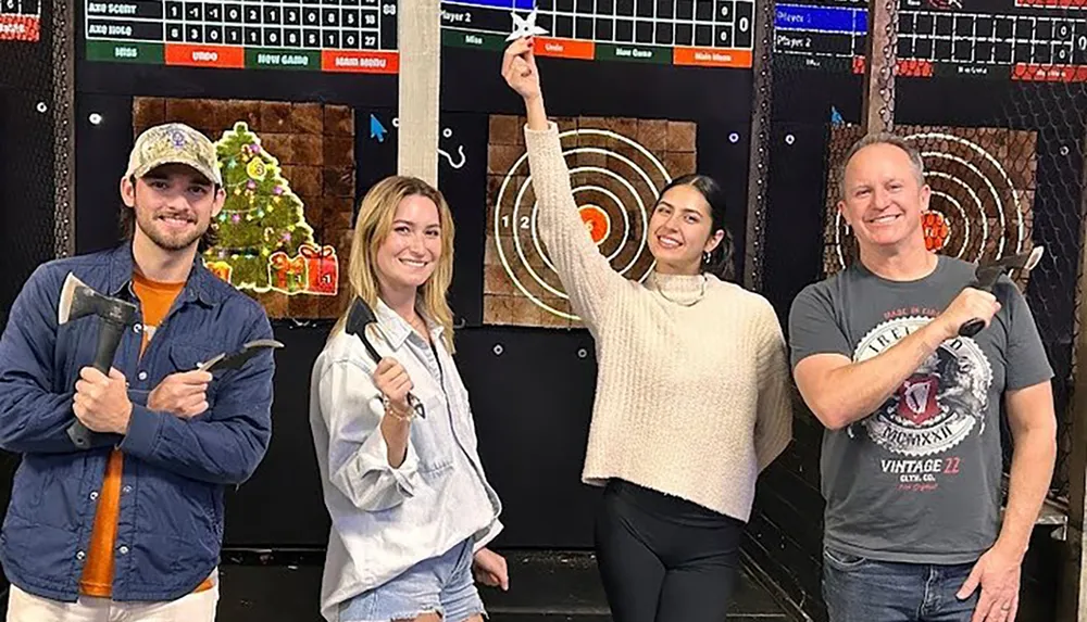 Four people are posing with axes in front of electronic axe-throwing targets with the middle person pointing at the bullseye they presumably hit