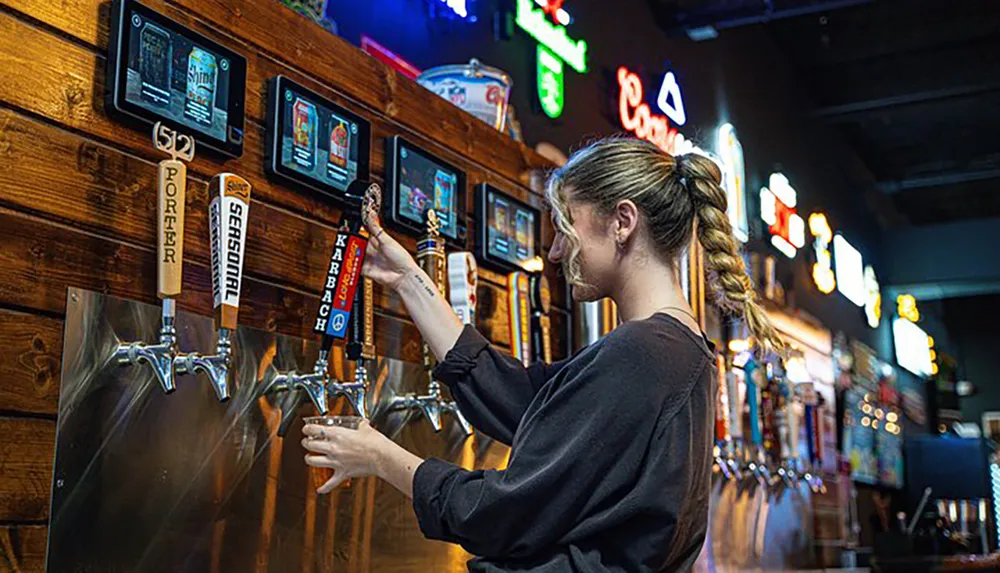 A bartender is pulling a beer tap to pour a drink in a bar with various beer options on tap