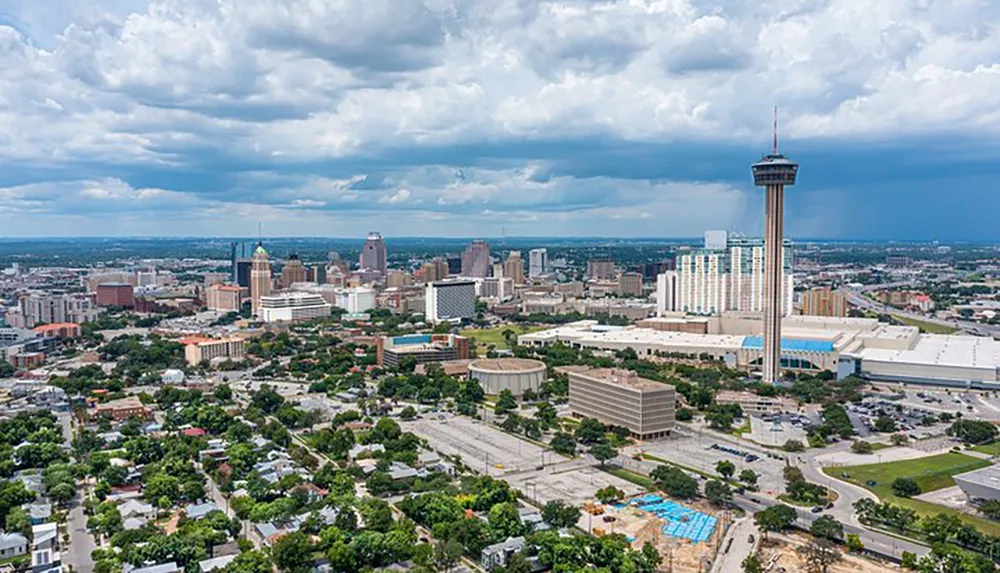 The image shows a panoramic view of a city skyline with a prominent tower under a cloudy sky