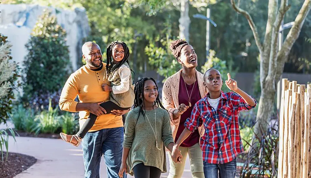 A happy family of four with a father carrying his daughter mother walking alongside their son is enjoying a sunny day outdoors in a park or garden