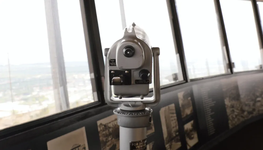 A coin-operated telescope is positioned inside a high-rise building offering expansive views of the surroundings