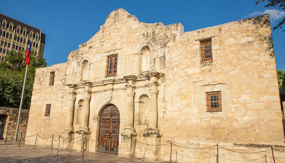 The image shows the historic Alamo mission in San Antonio Texas with its distinctive facade under a bright blue sky