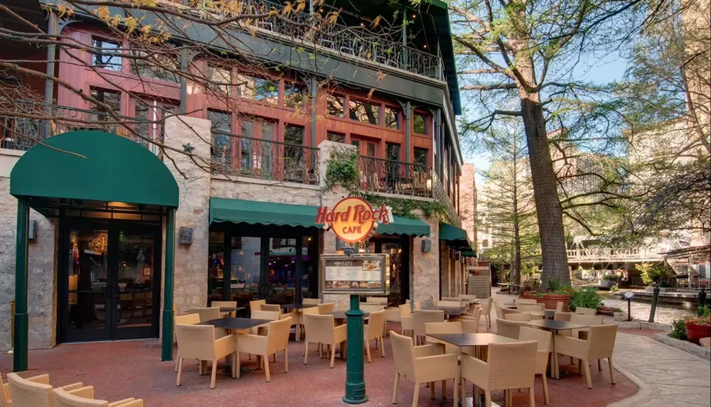 The image shows an outdoor seating area of a Hard Rock Caf by a tranquil pedestrian walkway lined with trees and brick buildings