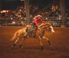 A rodeo rider is mounted on a bucking bull inside an arena surrounded by spectators and rodeo personnel