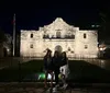 Three people are posing for a photo at night in front of the historic Alamo mission in San Antonio Texas illuminated by spotlights