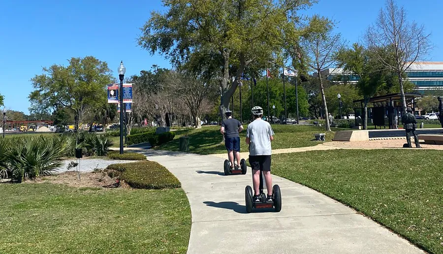 Two individuals are riding Segways along a park path on a sunny day.