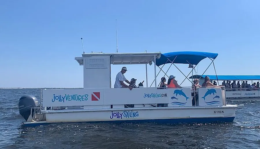 A group of people are enjoying a sunny day on a small boat with a blue canopy, named FLIPPER, and the side of the boat advertises JollyVentures with dolphin graphics.