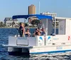 A group of individuals is enjoying a sunny day on a small pontoon boat against the backdrop of coastal buildings and clear blue skies