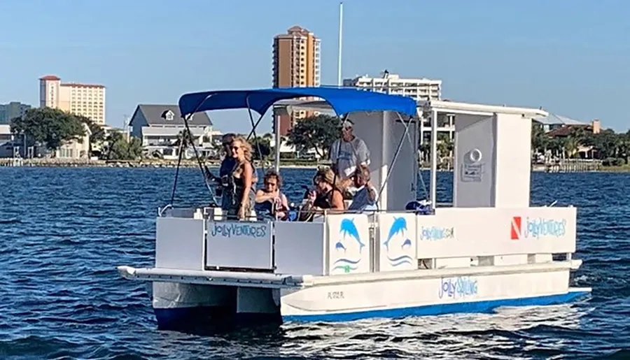 A group of individuals is enjoying a sunny day on a small pontoon boat against the backdrop of coastal buildings and clear blue skies.