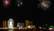 A nighttime cityscape featuring a lit Ferris wheel and brightly colored buildings is shown below a dark sky where multiple fireworks are displayed in separate insets.