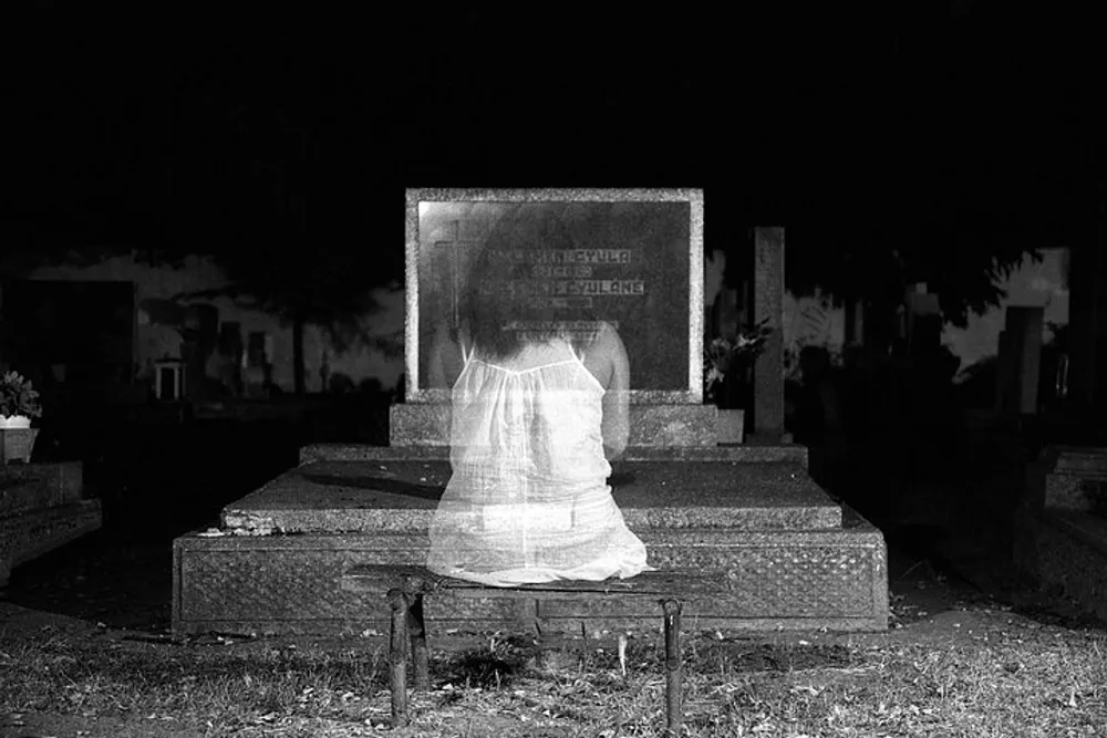 The image shows a transparent ghost-like figure seated in front of a tombstone in a dark graveyard evoking a supernatural or eerie atmosphere