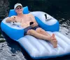 A person is relaxing on a blue and white inflatable raft in the water wearing sunglasses while holding a drink in one hand and a smartphone in the other