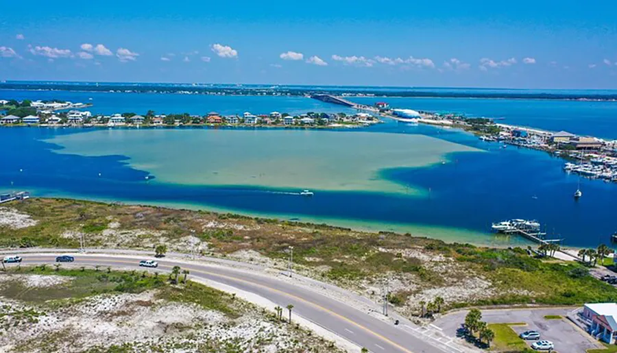 An aerial view of a coastal area showcasing a bridge connecting two land masses, with boat marinas and turquoise waters.