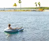 A person is relaxing on a blue and white inflatable raft in the water wearing sunglasses while holding a drink in one hand and a smartphone in the other