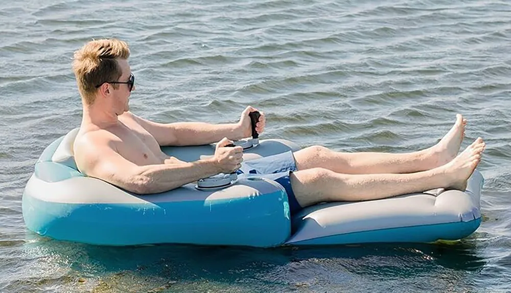 A person is lounging on an inflatable chair in the water holding a smartphone with their feet propped up