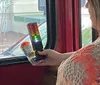 A person is holding a device with color-coded lights while sitting near a window possibly on a bus or train