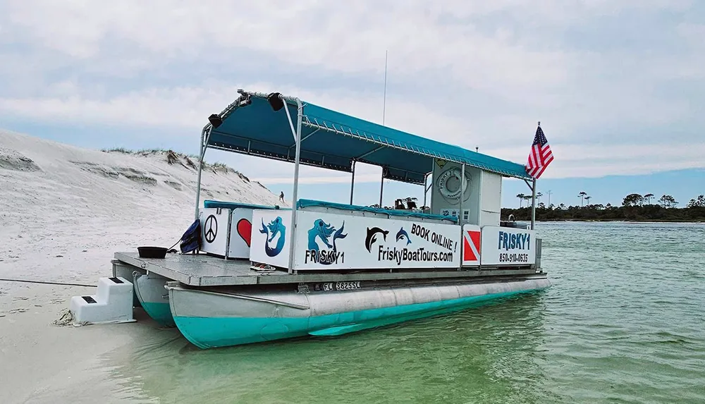 A tour boat named FRISKY1 is beached near a sand dune advertising boat tours with an American flag displayed on the rear