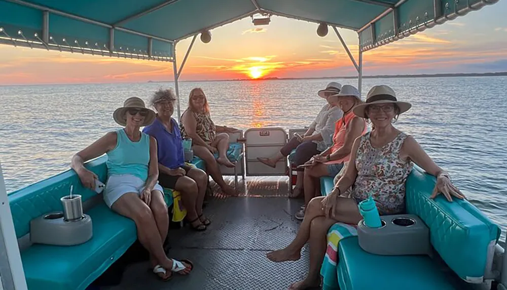 A group of smiling individuals is enjoying a boat ride at sunset surrounded by calm waters and a colorful sky