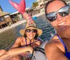 Two people are smiling for a selfie while floating on inflatables in the water with a beachfront building in the background