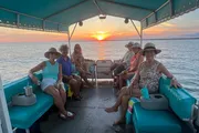 A group of people are enjoying a boat trip on the water at sunset.