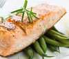 The image shows a group of people engaging in conversation at what appears to be a social event with a smaller inset picture of a salmon dish placed in the corner