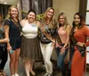 A group of women is smiling for the camera at what appears to be a pre-wedding celebration with some wearing sashes that read Bride Tribe and Bride set against a backdrop featuring Crime Scene Do Not Cross tape