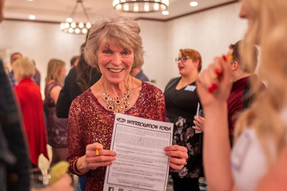 A smiling woman in a sparkly red top holds an Interrogation Form at a lively event with people socializing in the background