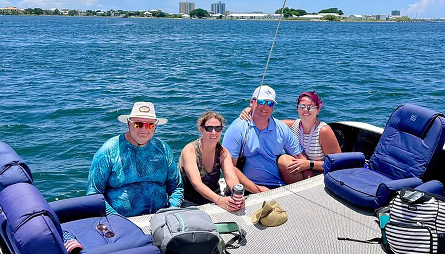 Four people are smiling for a photo while sitting on a pontoon boat on a sunny day with calm blue waters in the background.