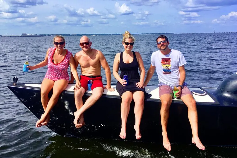 Four friends are sitting on the edge of a boat enjoying a sunny day on the water