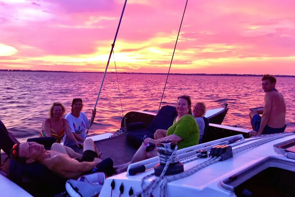 A group of people is enjoying a serene boat ride at sunset with vivid pink and purple skies reflecting on the water