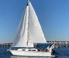 A sailboat with its sails unfurled glides across blue water near a long pier under a clear sky